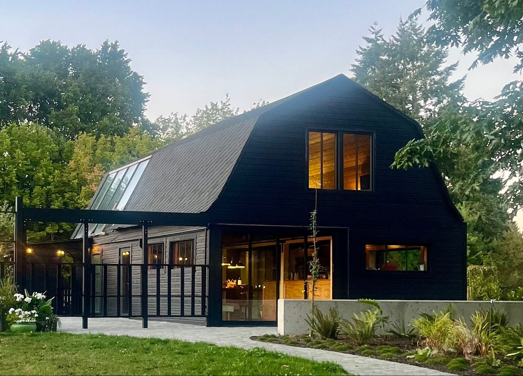 Modern black barn with large windows in a green, tree-lined area