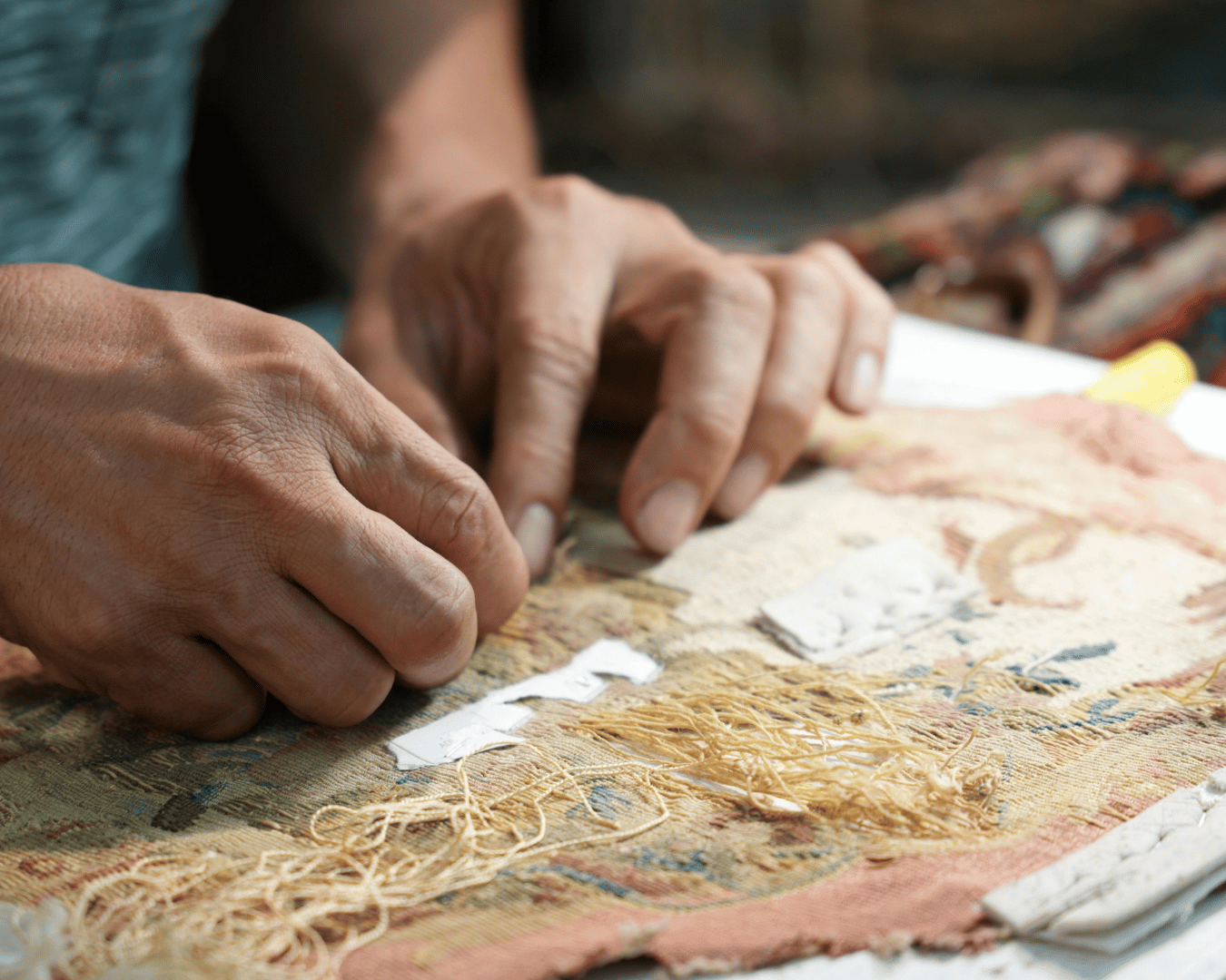 Close-up of hands working on repairing an old rug with visible threads and fabric.