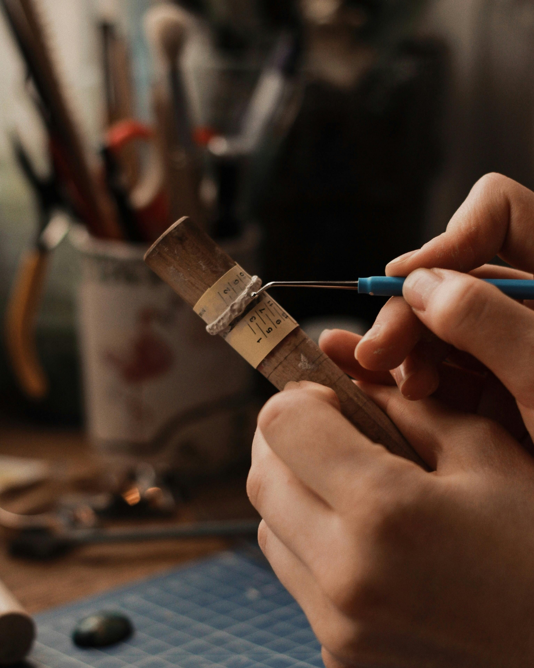Person using a tool on a wooden object with a blurred workshop background